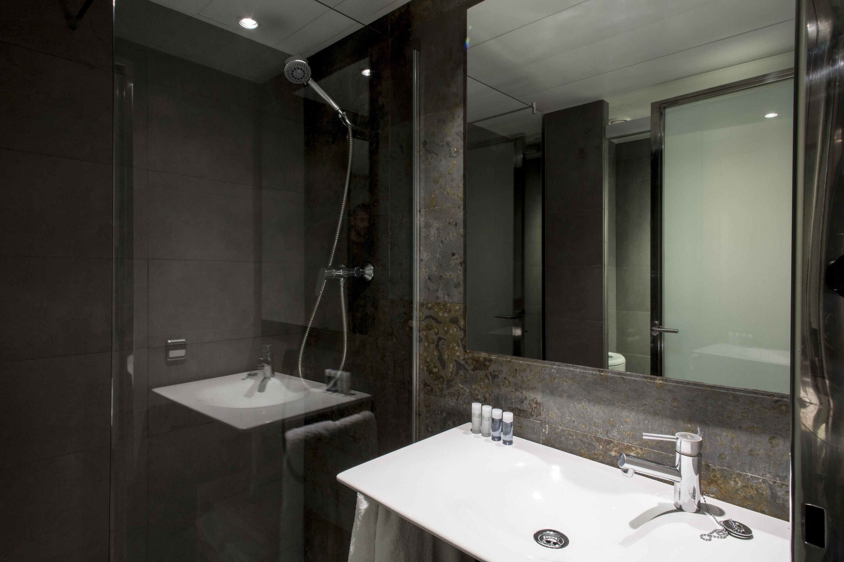 A modern bathroom with a glass-enclosed shower, a white sink, and a large mirror.