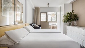 A hotel room with a large bed, a desk, a chair, a plant, and a window with curtains. - Aramunt Apartments (Barcelona)