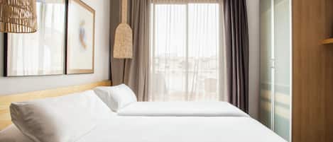 Een hotelkamer met een bed, een kledingkast, een hanglamp en een raam met gordijnen.