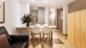 A modern dining area with a wooden table, two chairs, a potted plant, and a black leather couch. - Aramunt Apartments (Barcelona)