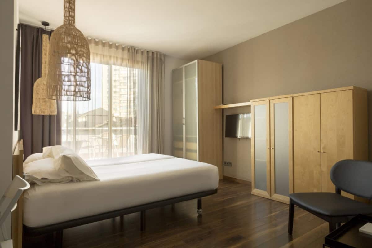 A bedroom with a bed, a wardrobe, a chair, and a hanging light fixture.