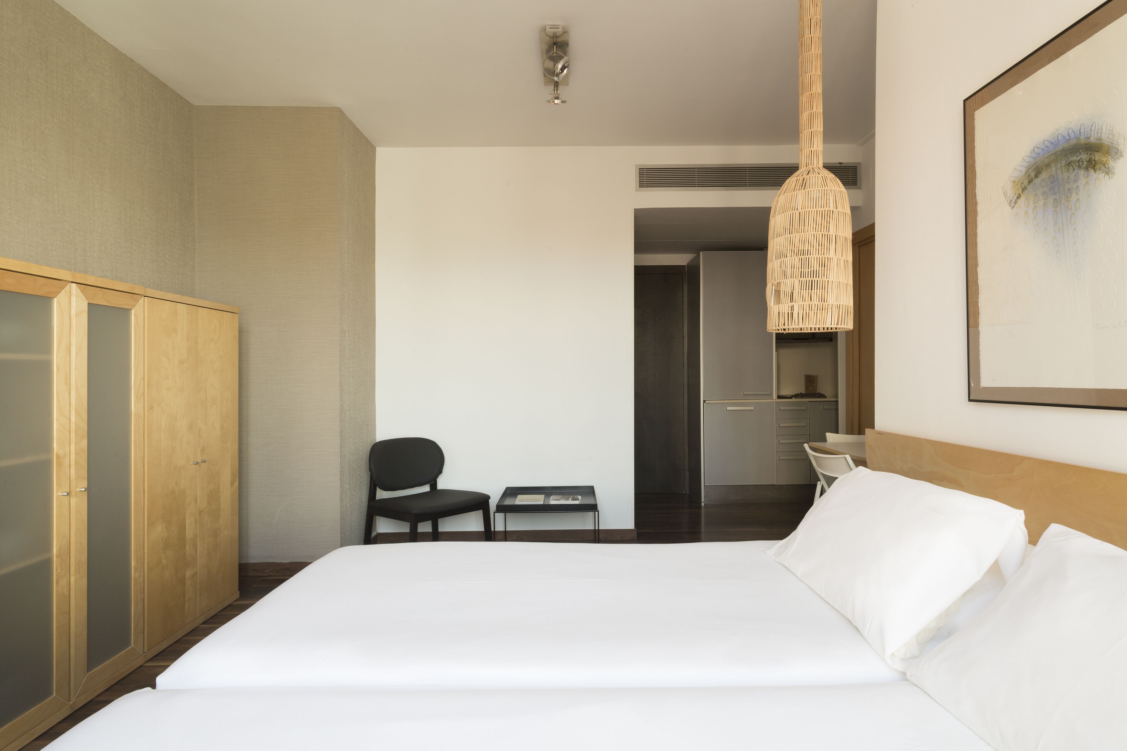A hotel room with a bed, a wardrobe, a chair, a small table, and a hanging light fixture.