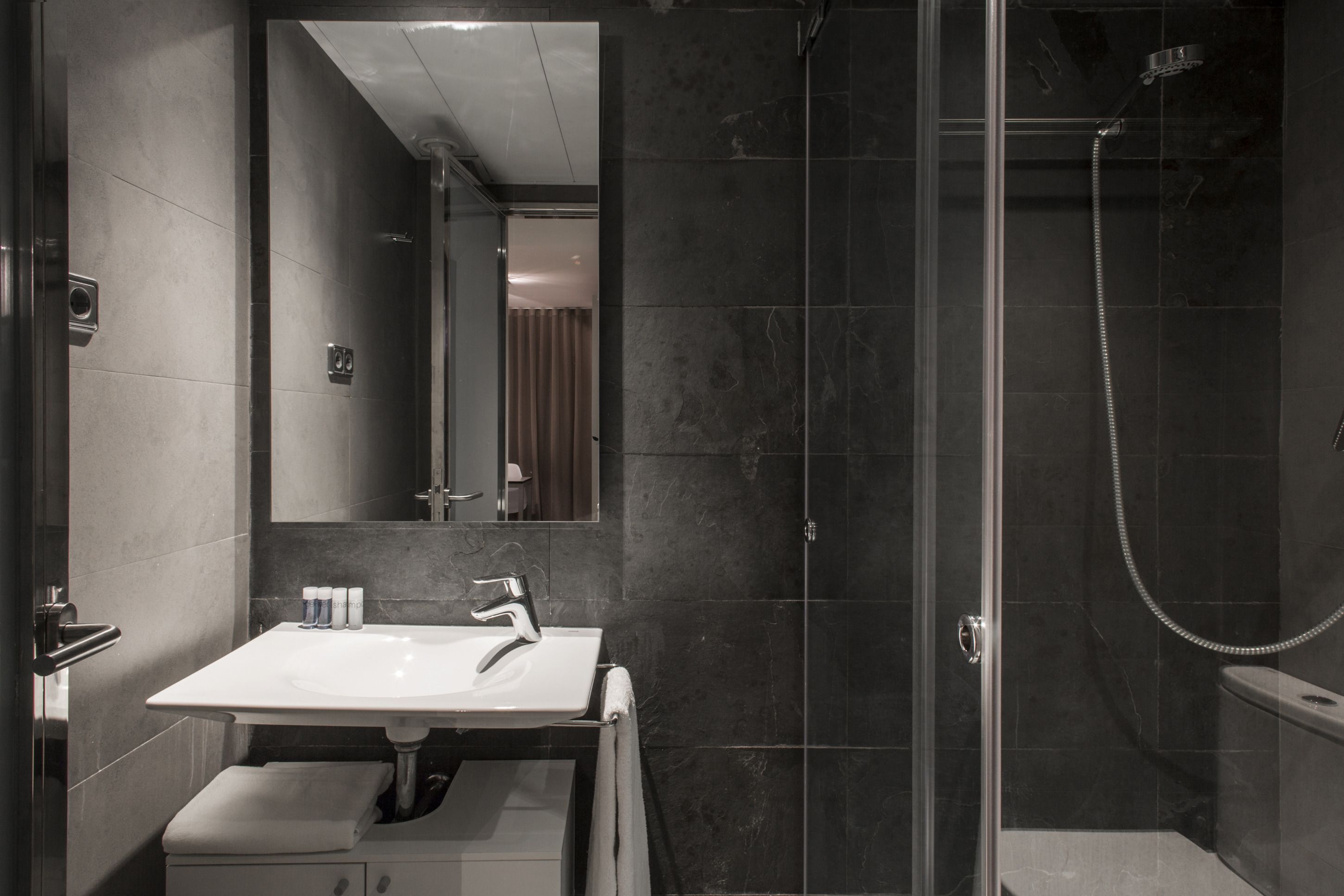 A modern bathroom with a white sink, a large mirror, and a glass-enclosed shower area.
