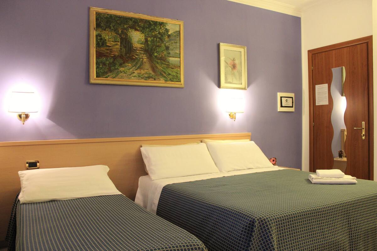 A hotel room with two beds, a painting, and a door with a mirror.