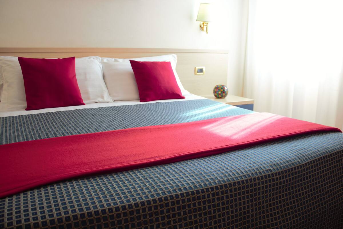 A neatly made bed with a blue and red bedspread, white pillows, and a red throw blanket.