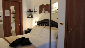 A hotel room with a bed, a nightstand, a mirror, and a door. - Città Eterna Bed & Breakfast (Rome)