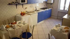 A kitchen with blue cabinets, a white microwave, and a dining table set with plates, cups, and a fruit bowl. - Città Eterna Bed & Breakfast (Rome)