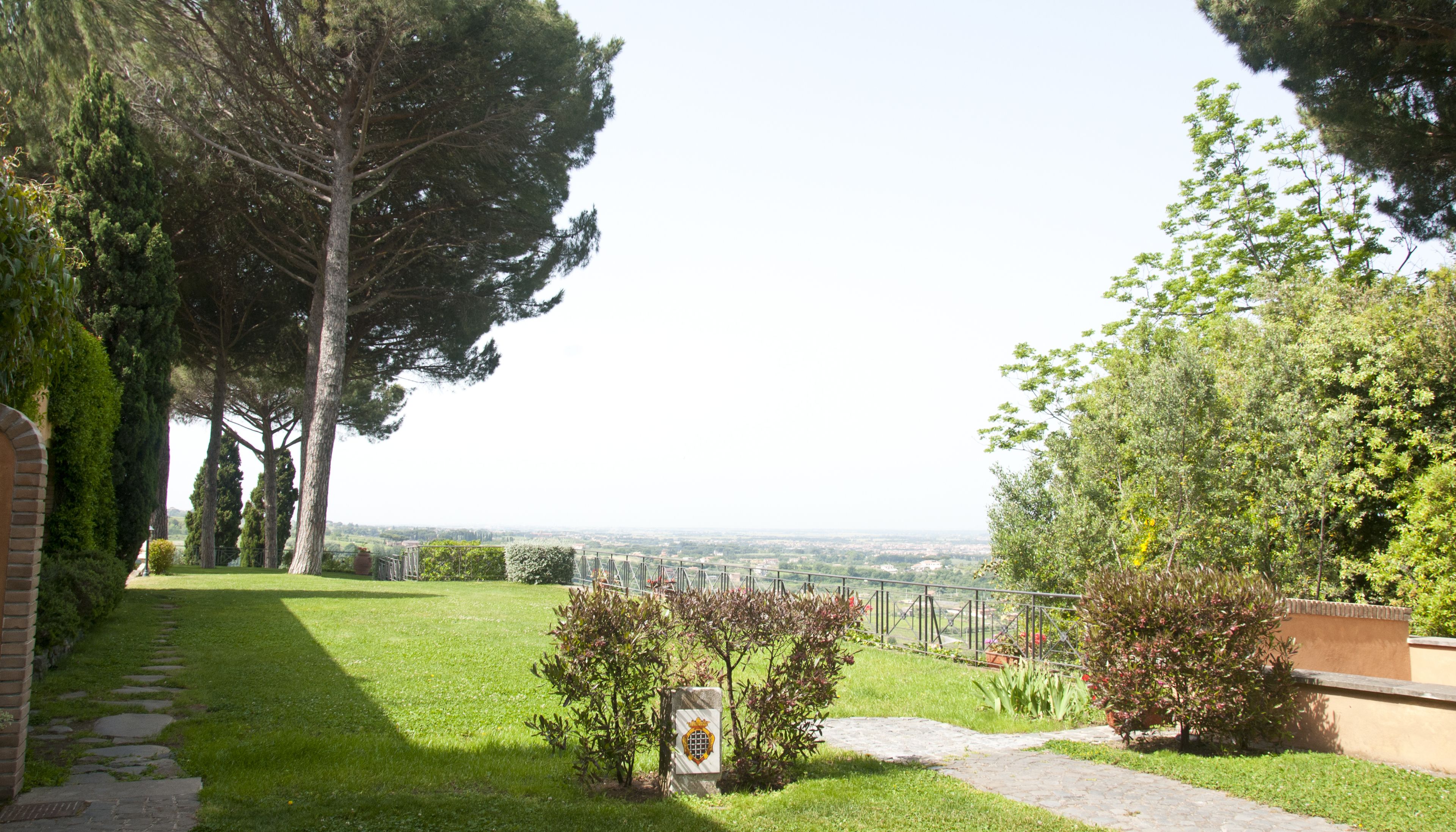 A garden with a paved path, a stone wall, and a view of the city in the distance.