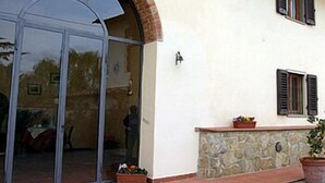 A building with a large glass door entrance, stone wall, and a small planter with flowers. - Il Colombaino (Scandicci)
