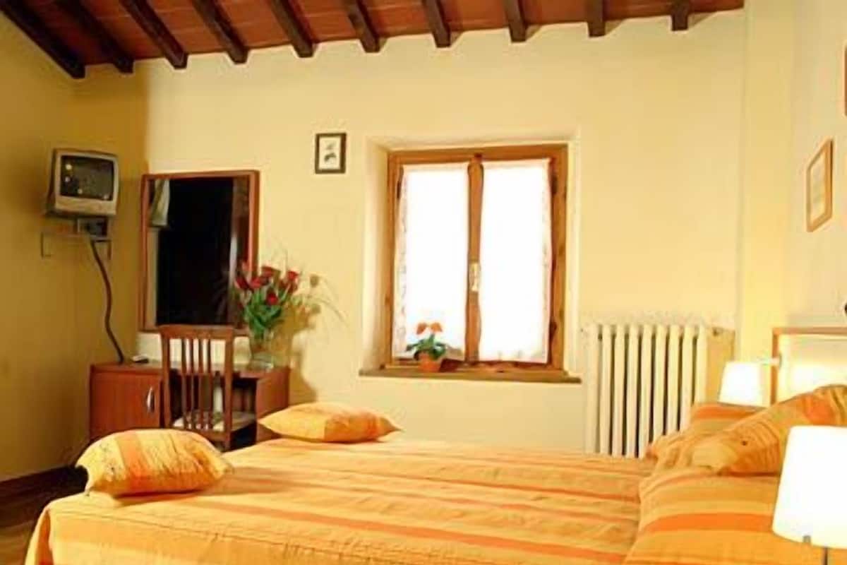 A bedroom with a bed, a desk, a chair, a window, and a radiator.