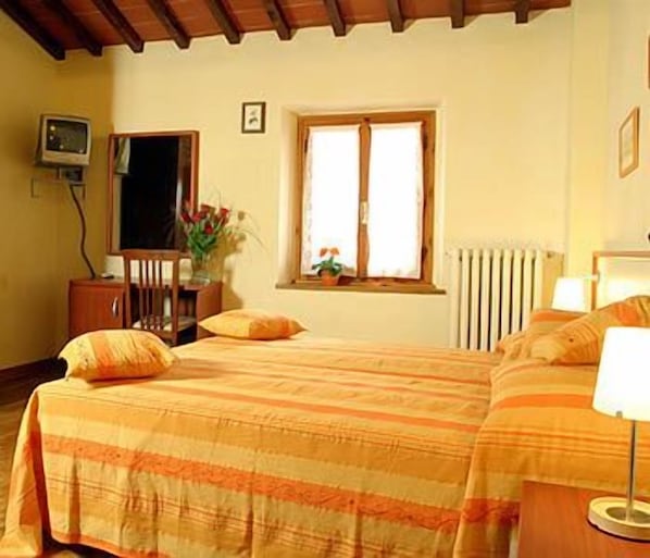 A bedroom with a bed, a desk, a chair, a window, and a radiator. - Il Colombaino (Scandicci)