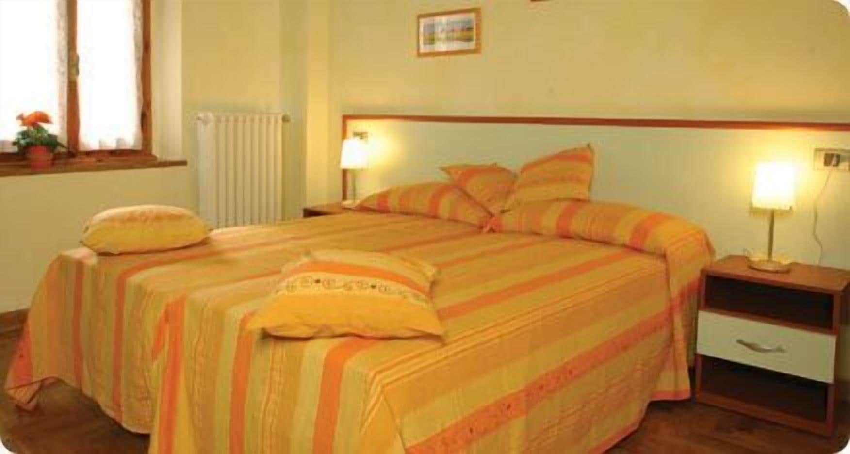 Una cama doble con ropa de cama a rayas, una mesita de noche con lámpara y una ventana con cortinas.