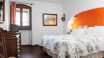 A bedroom with a wooden dresser, a bed with a floral bedspread, a framed picture on the wall, and a window with curtains.