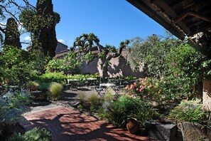 A garden with a brick pathway, potted plants, and outdoor seating. - Hotel Lucrezia (Riola Sardo)