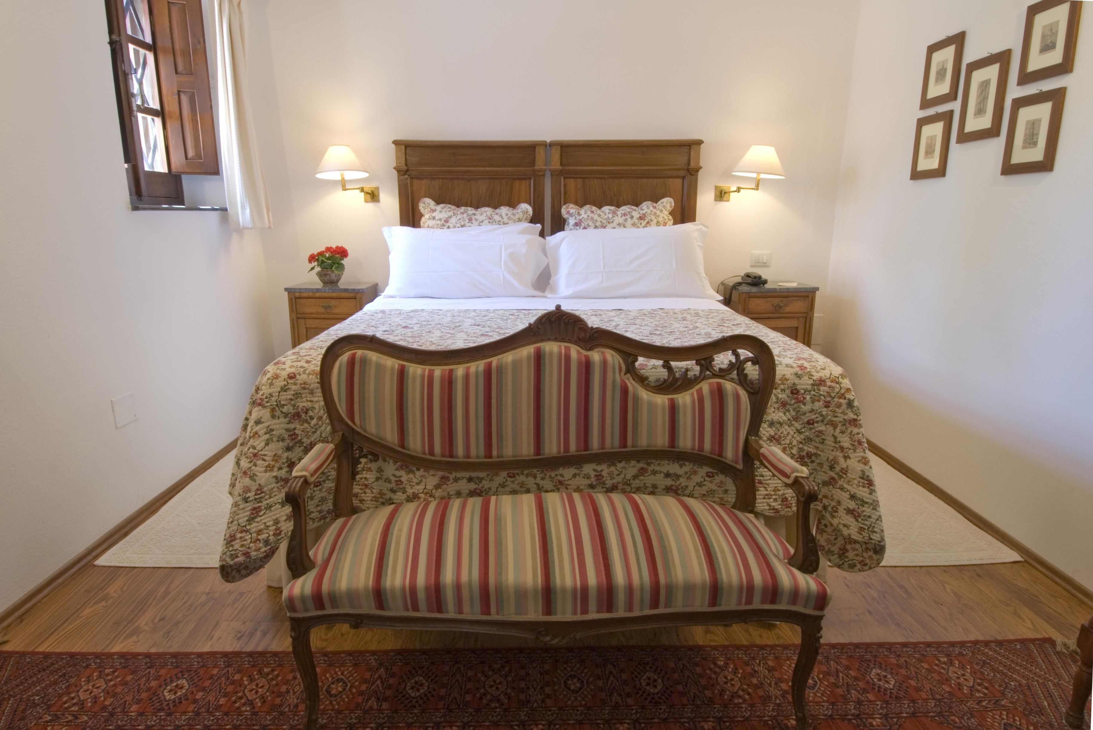 Une chambre à coucher bien rangée, avec un lit, deux tables de chevet, une chaise et une petite table sur laquelle est posé un vase de fleurs.