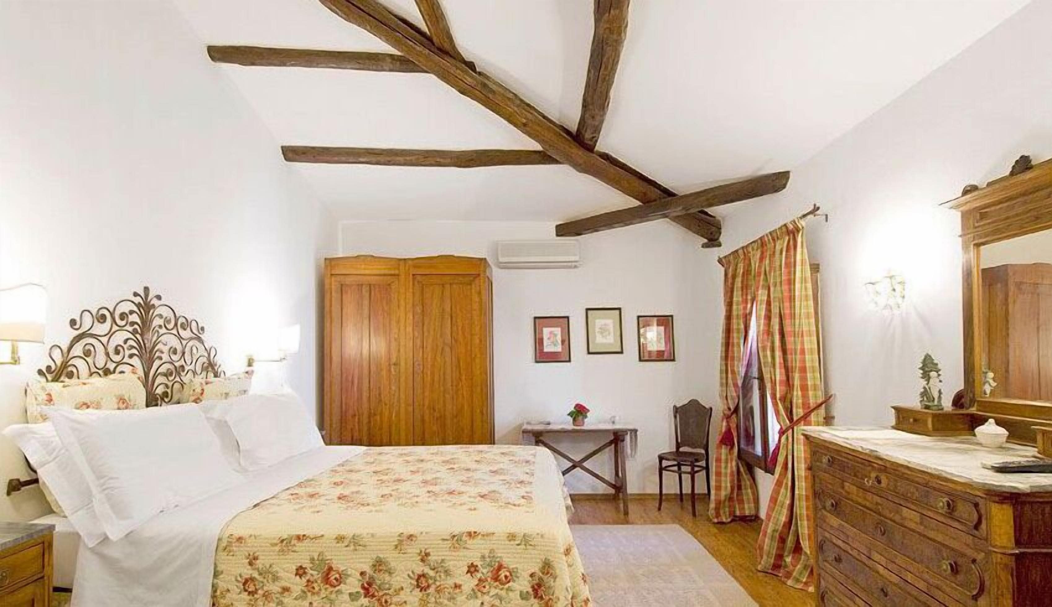 A bedroom with a bed, wooden wardrobe, desk, chair, dresser, and a mirror.