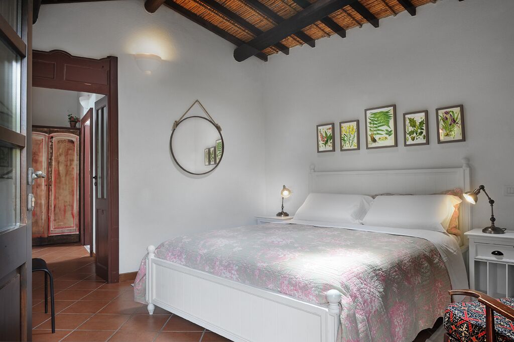 Une chambre à coucher avec un lit, des lampes de chevet, un miroir et des reproductions encadrées de motifs botaniques accrochées au mur.