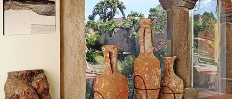 A room with terracotta pots, a wooden sculpture, and a glass door leading to an outdoor area with plants and a view of a rocky landscape.