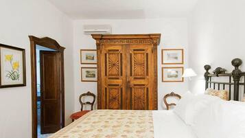 Quarto com guarda-roupa de madeira, cama com roupa de cama florida, uma cadeira e quadros nas paredes.