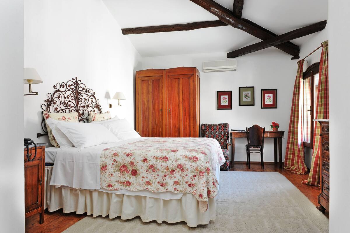 A bedroom with a bed, wooden wardrobe, desk, chair, and a window with curtains.