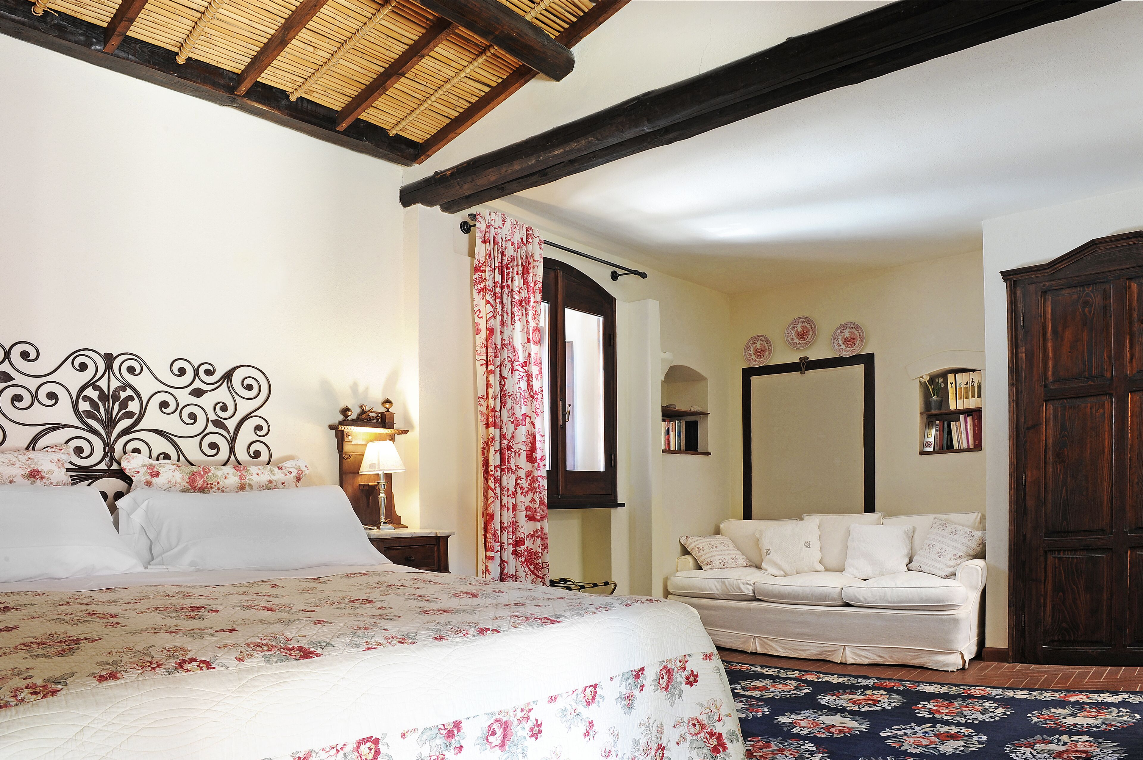 A bedroom with a bed, a nightstand, a dresser, a window with curtains, and a sofa.