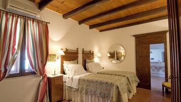 Un dormitorio con dos camas, vigas de madera en el techo, una ventana con cortinas, una mesita de noche con lámpara y un espejo en la pared.