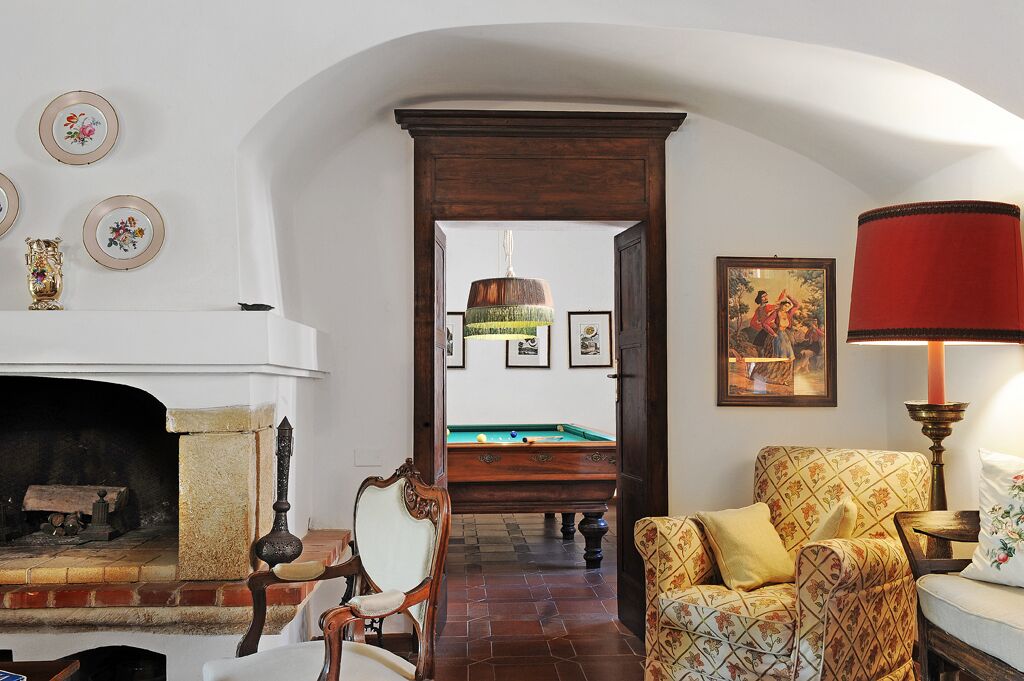 A room with a fireplace, a billiards table, and a red lamp.