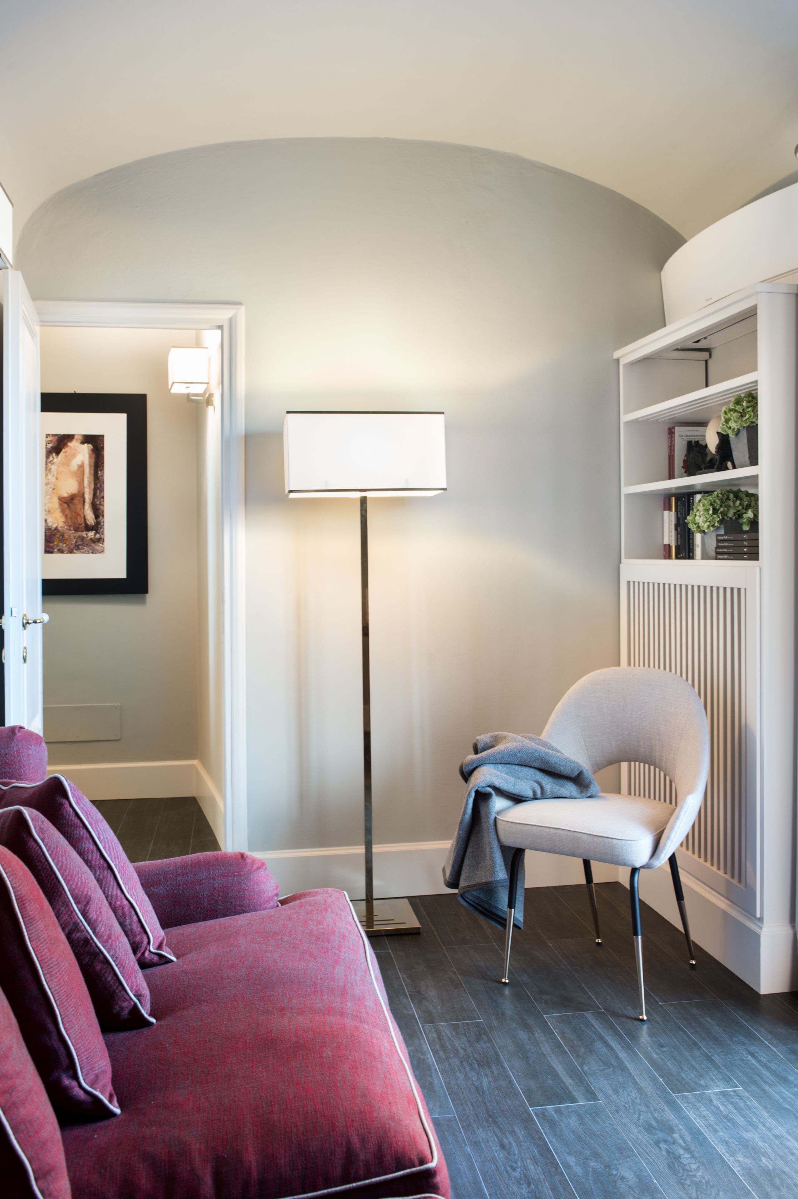 Un couloir avec un canapé rouge, une chaise blanche, un lampadaire et une bibliothèque.