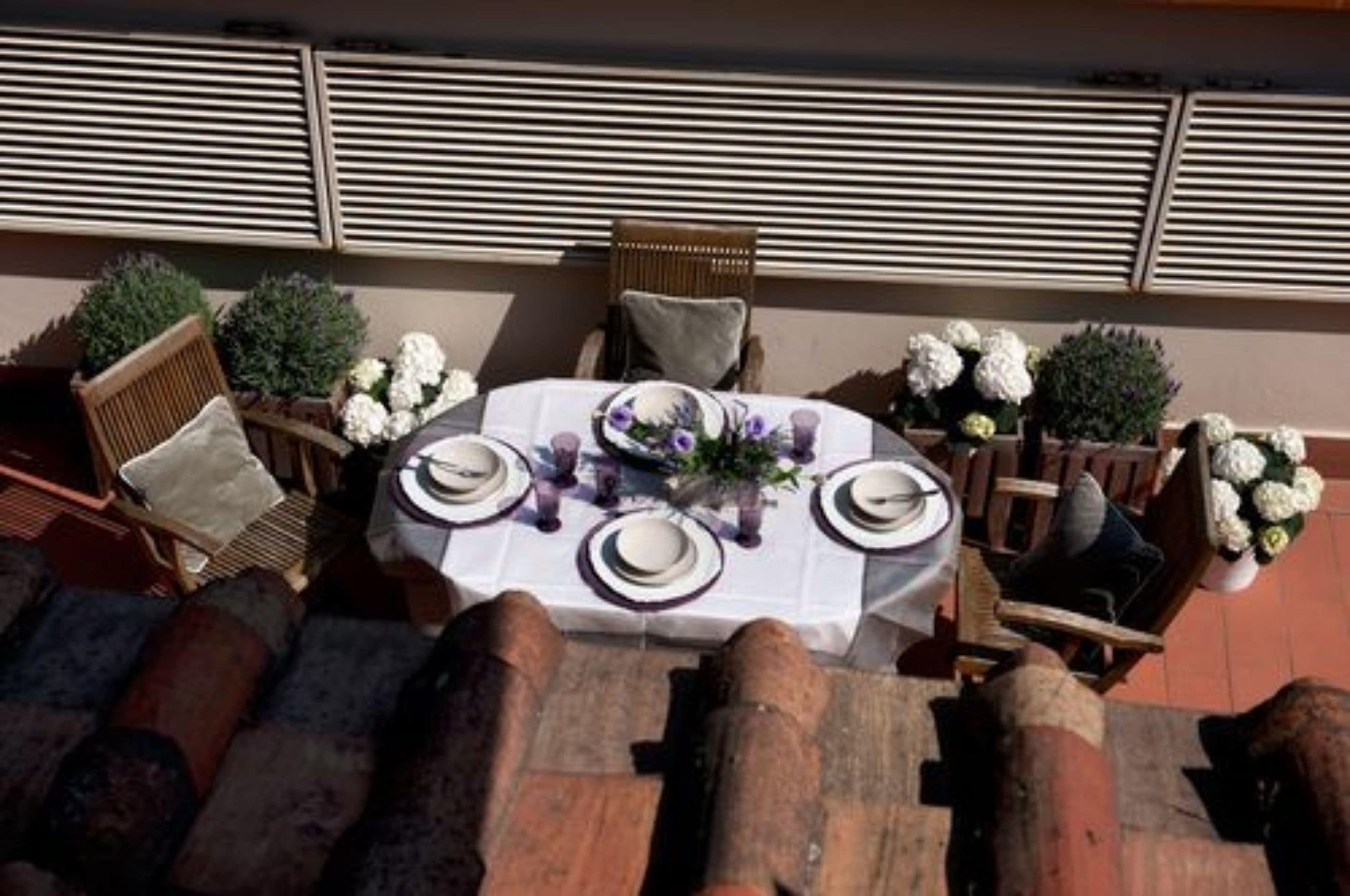 An outdoor dining area with a round table set for four, surrounded by wicker chairs and potted plants.