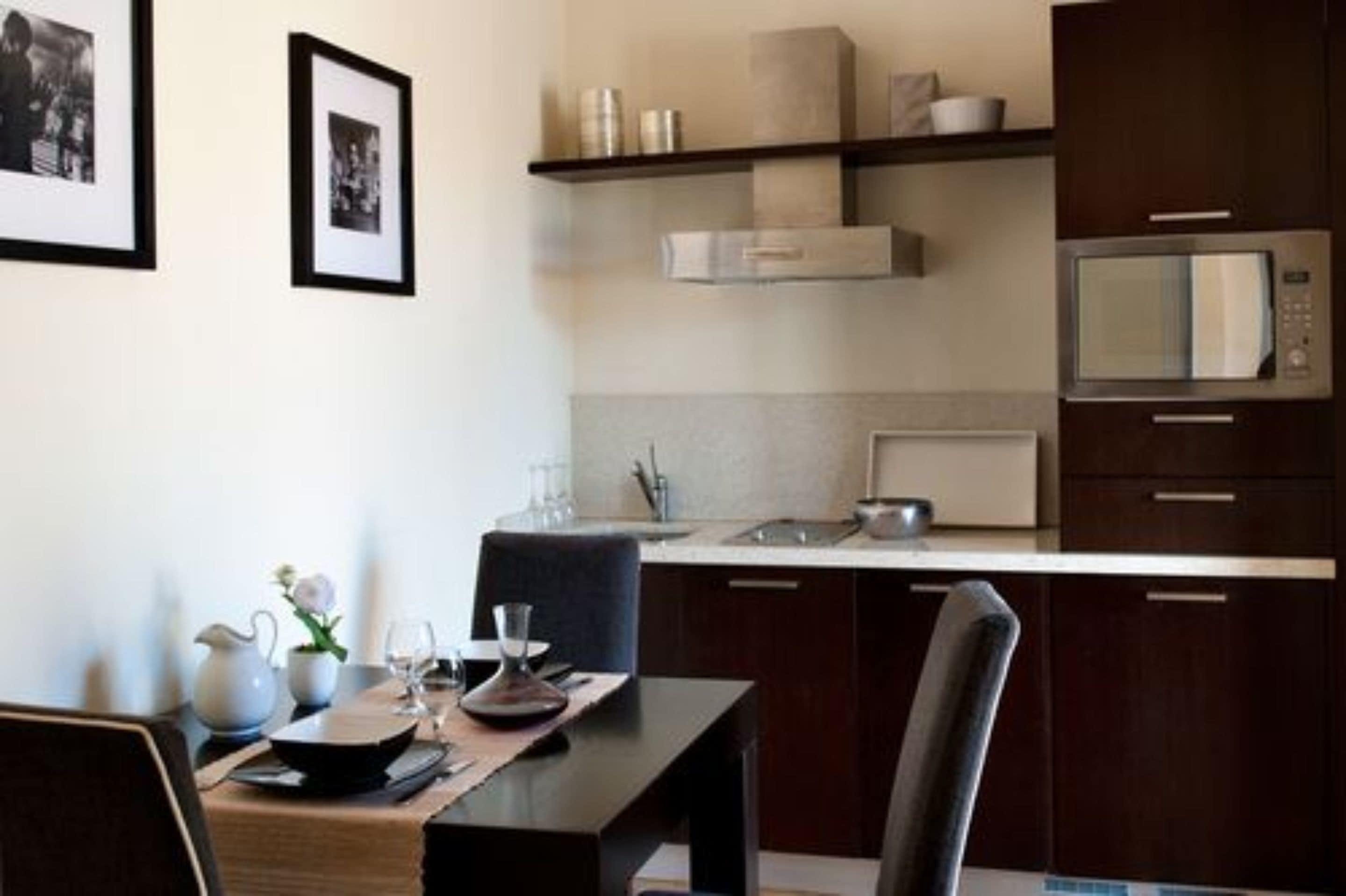 Een moderne keuken met donkere houten kastjes, een stalen magnetron en een eethoek met een tafel gedekt voor twee personen.