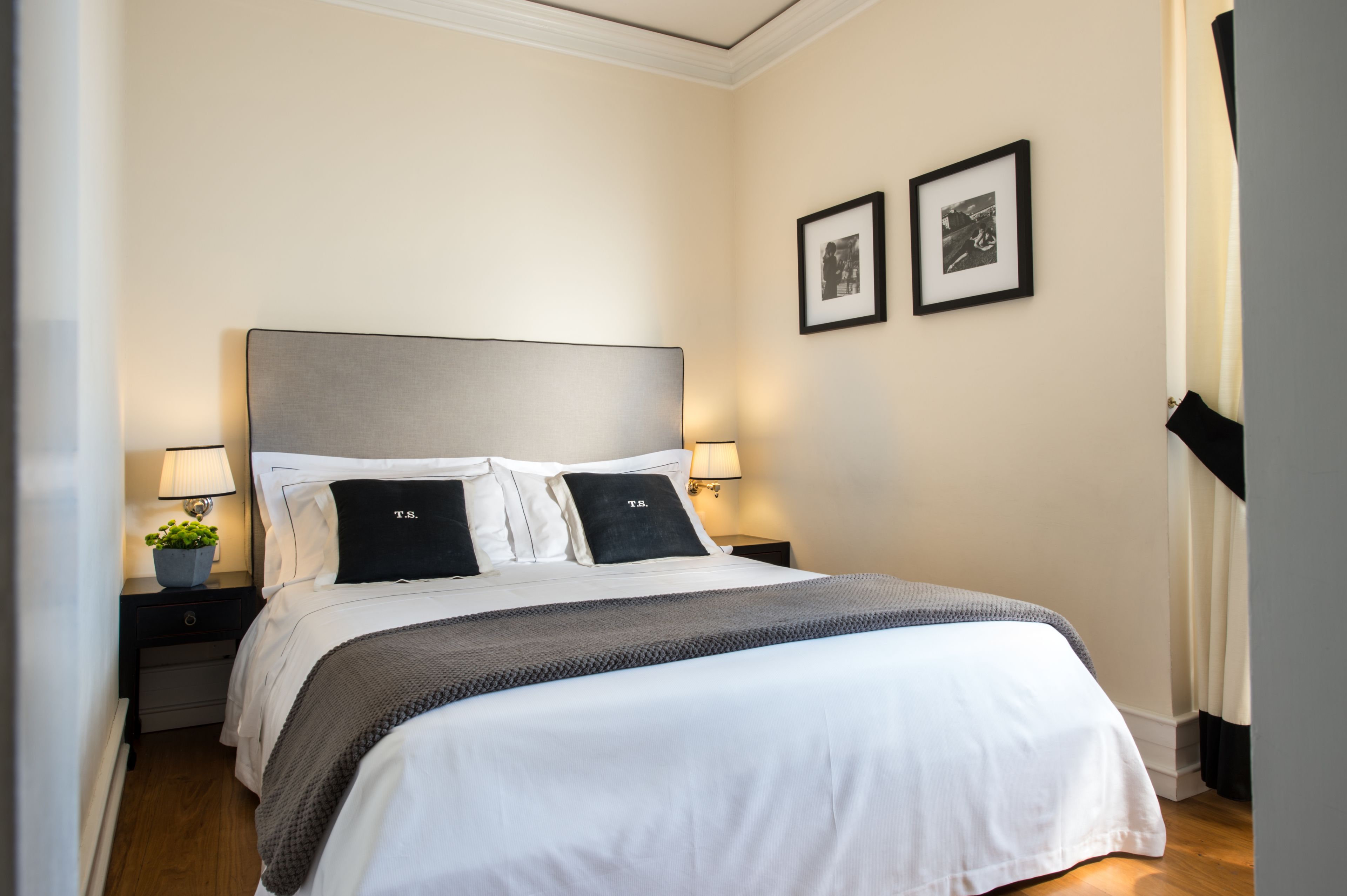 A neatly made bed with a grey headboard, two bedside tables with lamps, and two framed pictures on the wall.