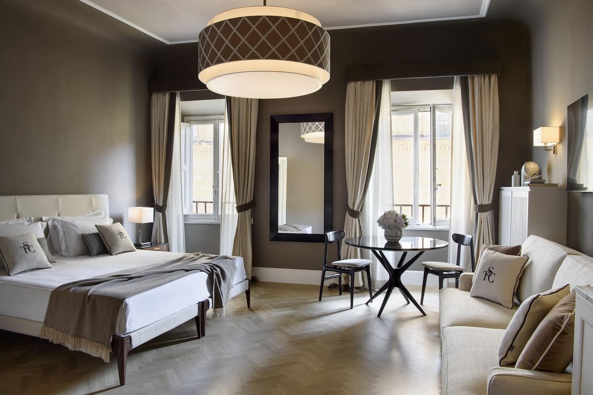 Quarto de hotel com uma cama grande, um sofá, uma mesa de jantar e um candelabro.