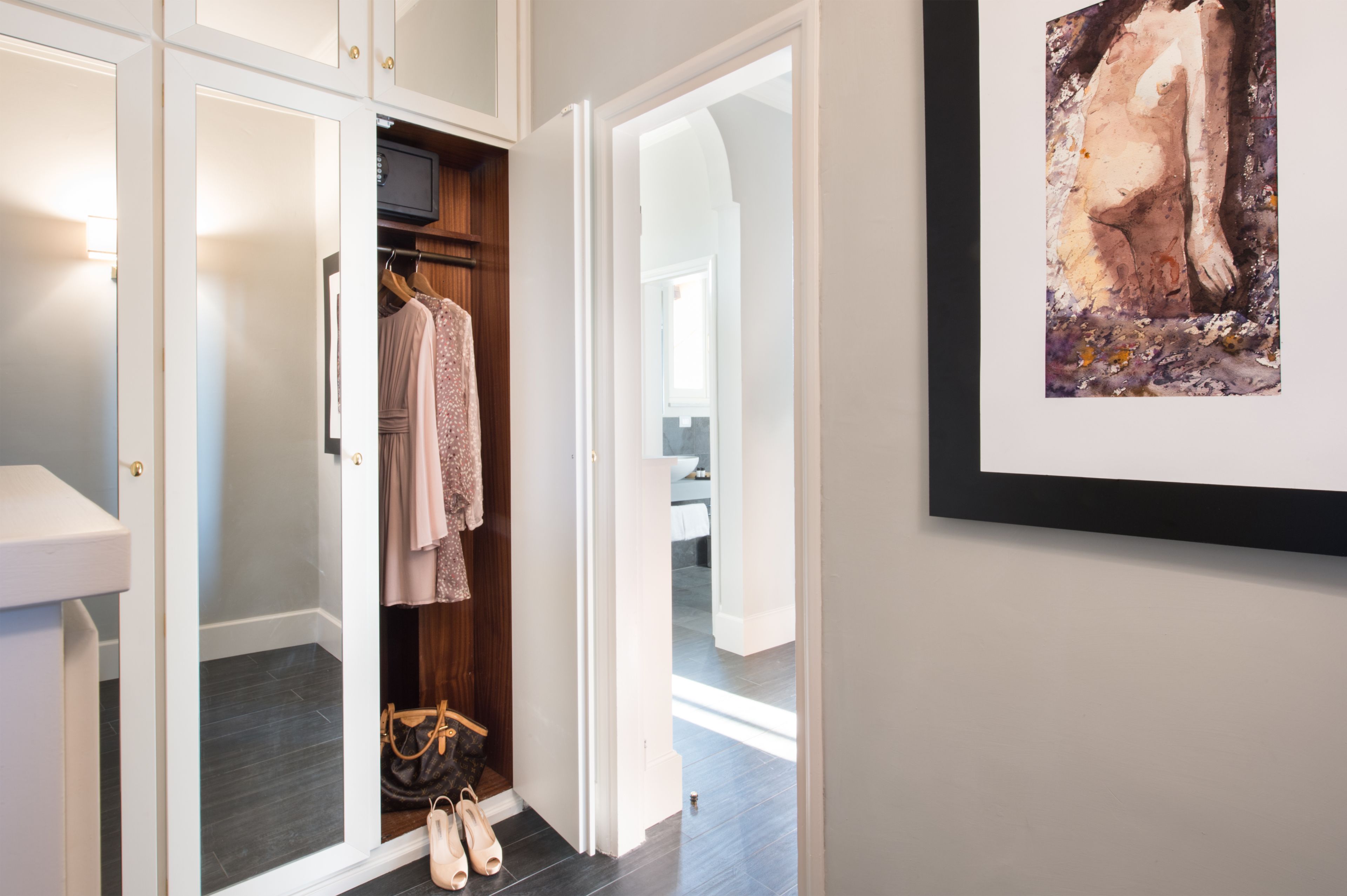 A walk-in closet with hanging clothes and a handbag on the floor.