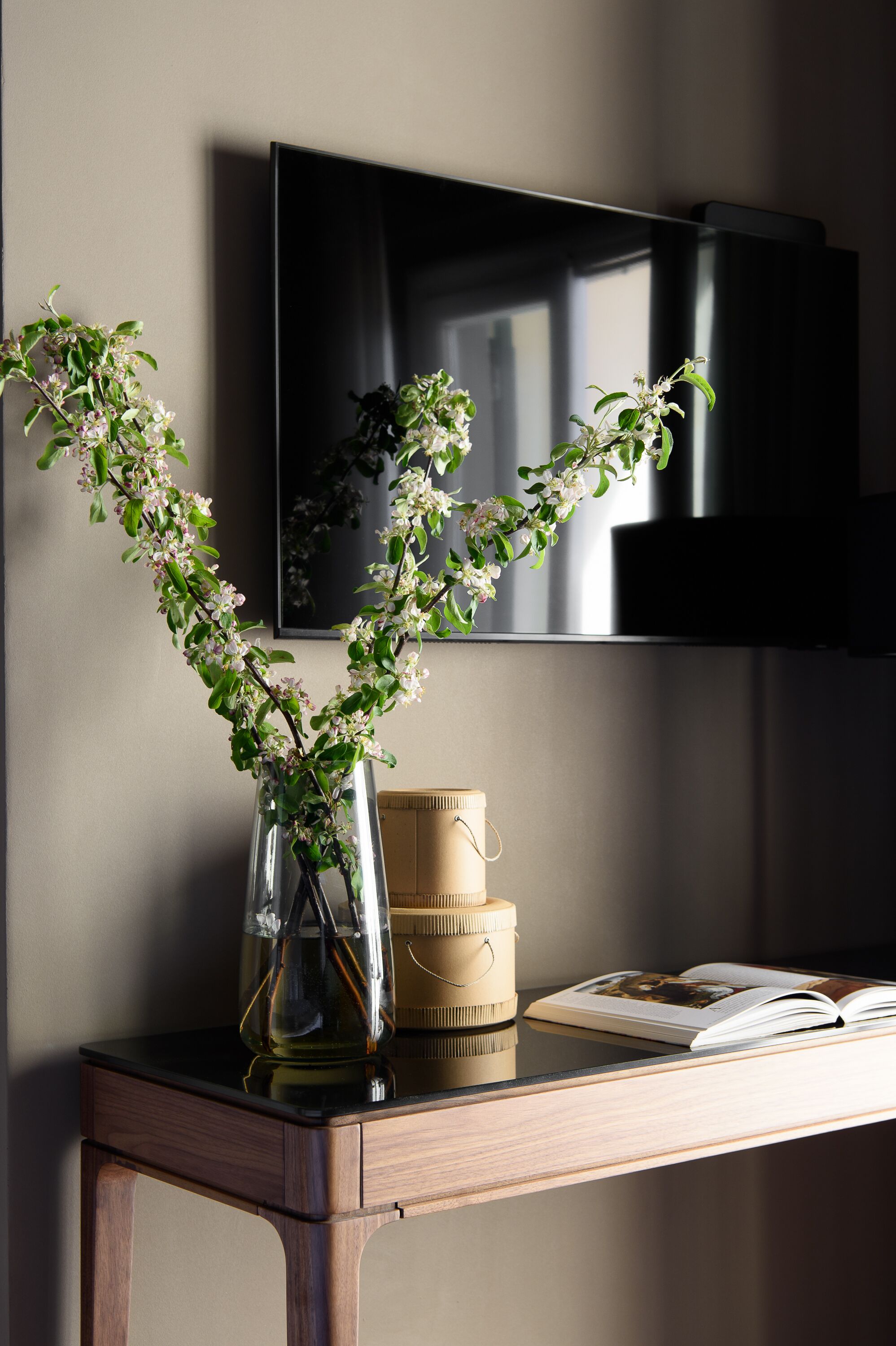 A wooden table with a vase of flowers, a book, and stacked containers.