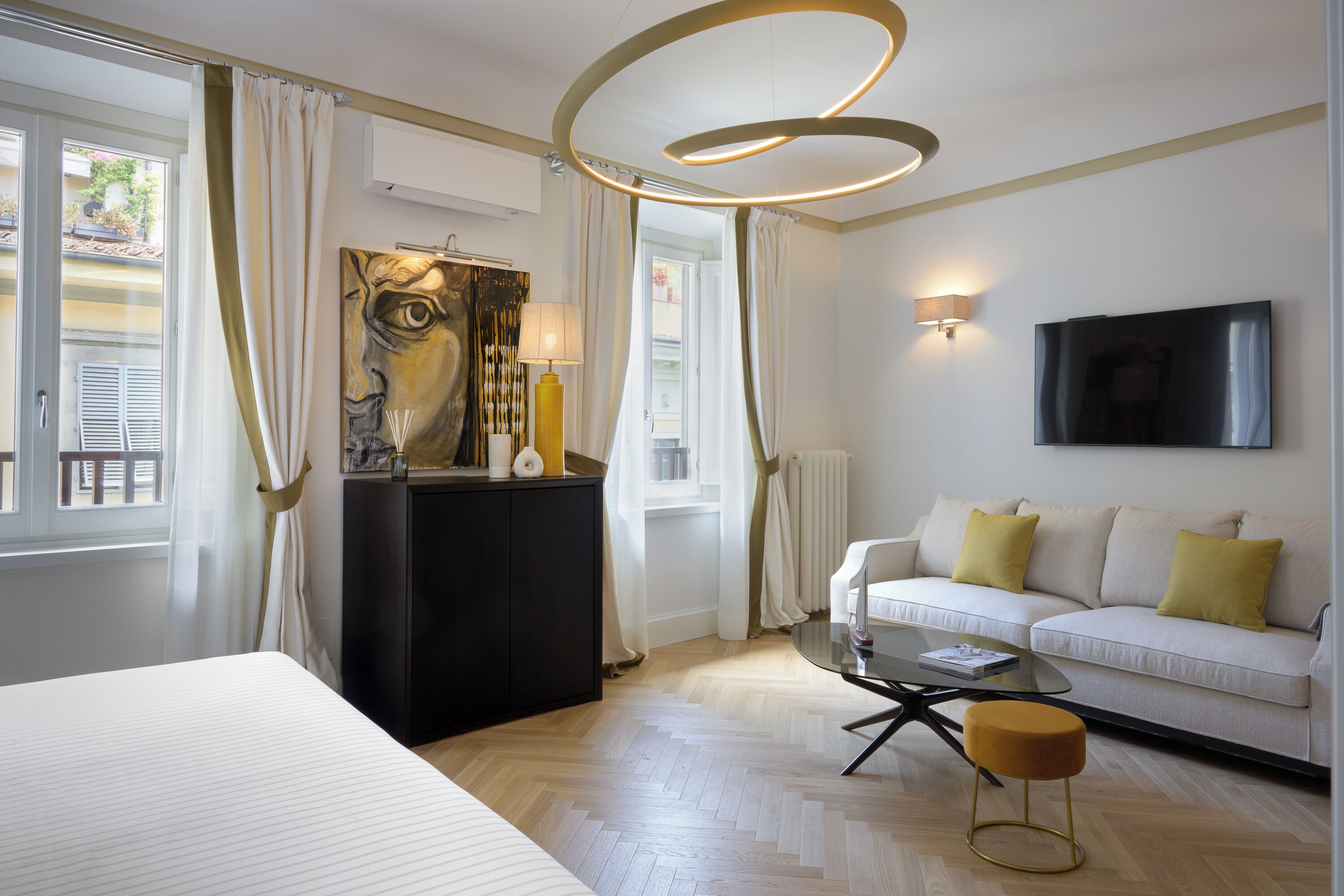 A hotel room with a bed, a sofa, a coffee table, a painting, and a TV.