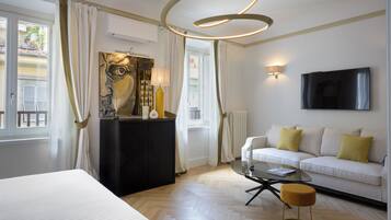 A hotel room with a bed, a sofa, a coffee table, a painting, and a TV.