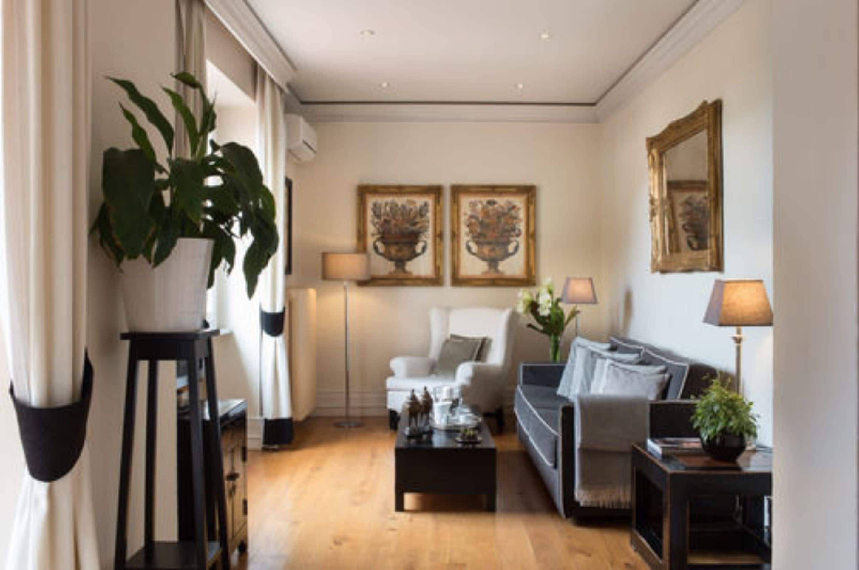 Sala de estar com sofá, poltronas, mesa de centro e luminária de chão. Há duas pinturas na parede e um vaso com planta.