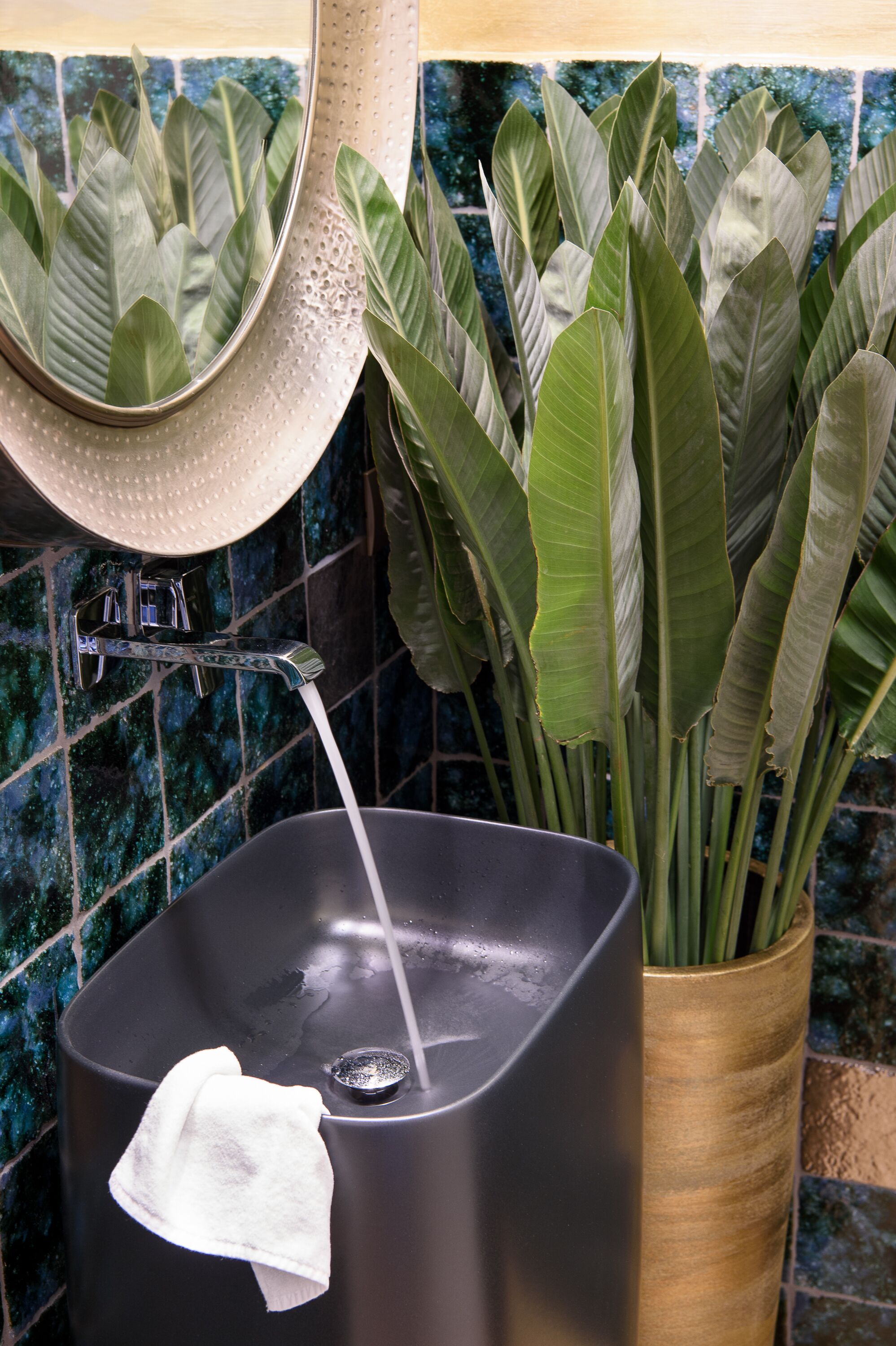 Une salle de bain avec un lavabo noir, une serviette blanche et une plante décorative dans un vase en bois.