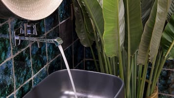 Une salle de bain avec un lavabo noir, une serviette blanche et une plante décorative dans un vase en bois.