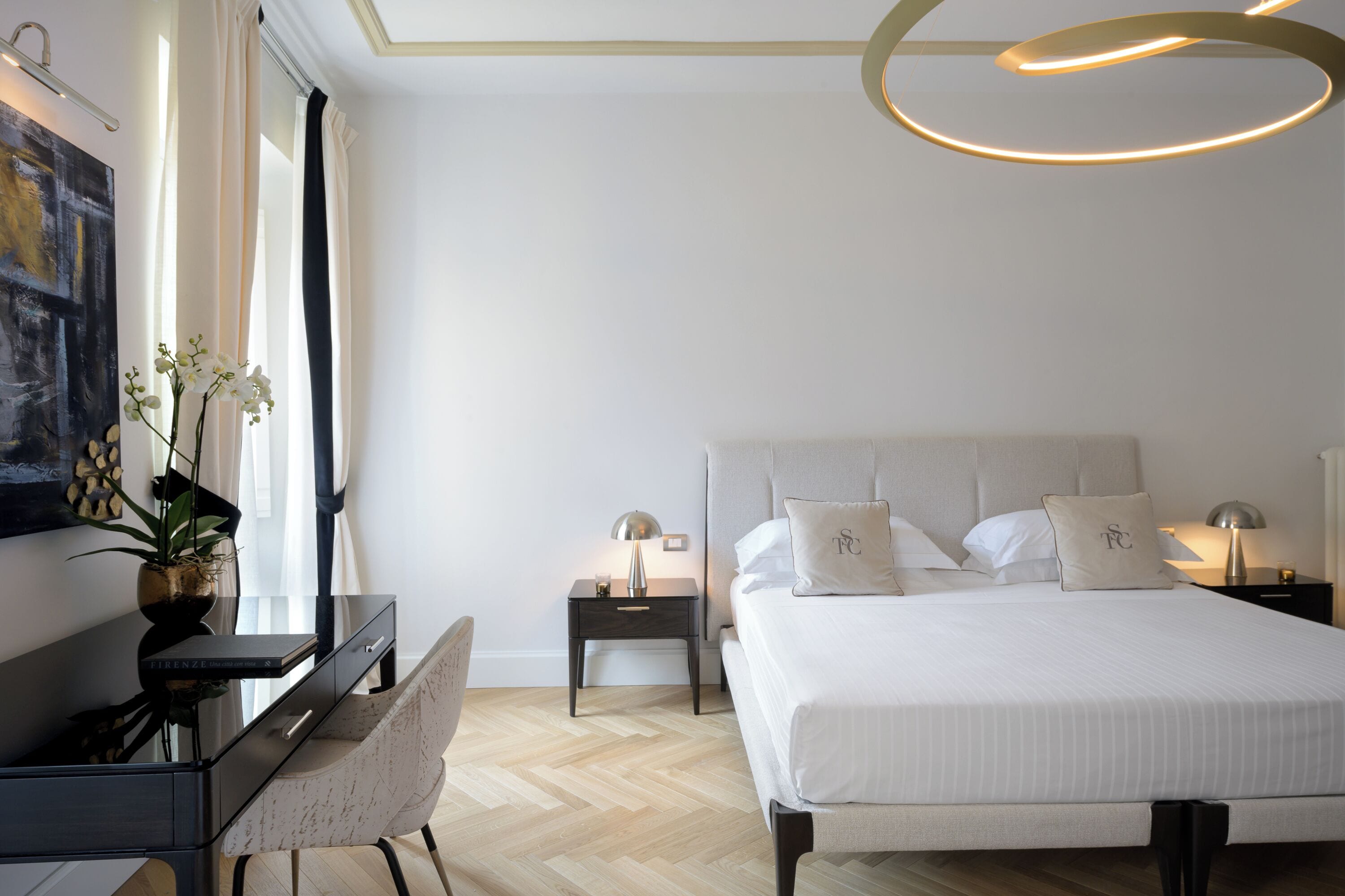 A modern bedroom with a large bed, bedside tables, a desk, and a chair.