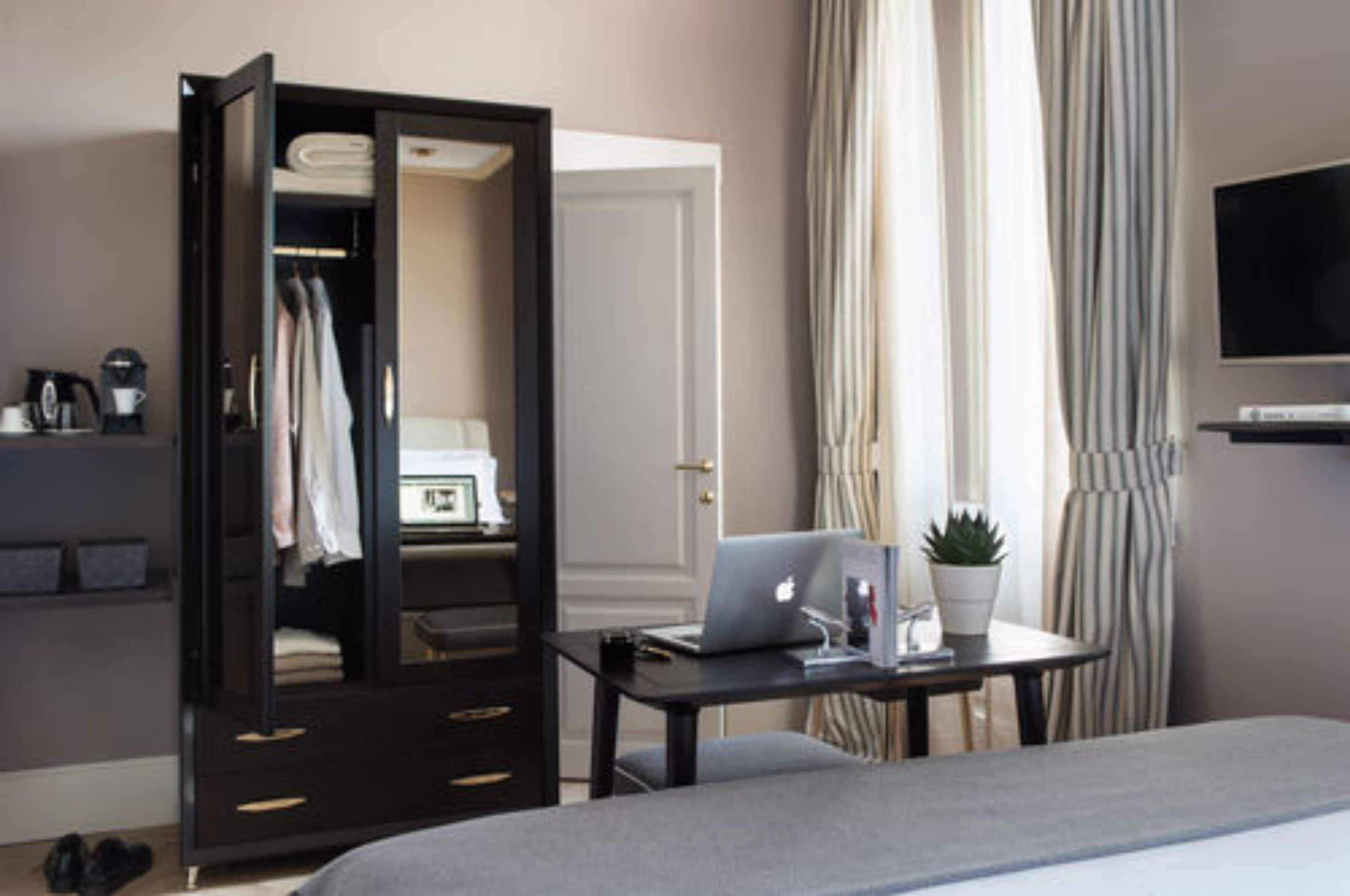 Ein Hotelzimmer mit Bett, Schreibtisch mit Laptop, Kleiderschrank, Fernseher und einer Topfpflanze.