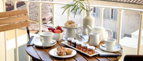 A balcony with a table set for tea, a vase with a plant, and a view of a cityscape.