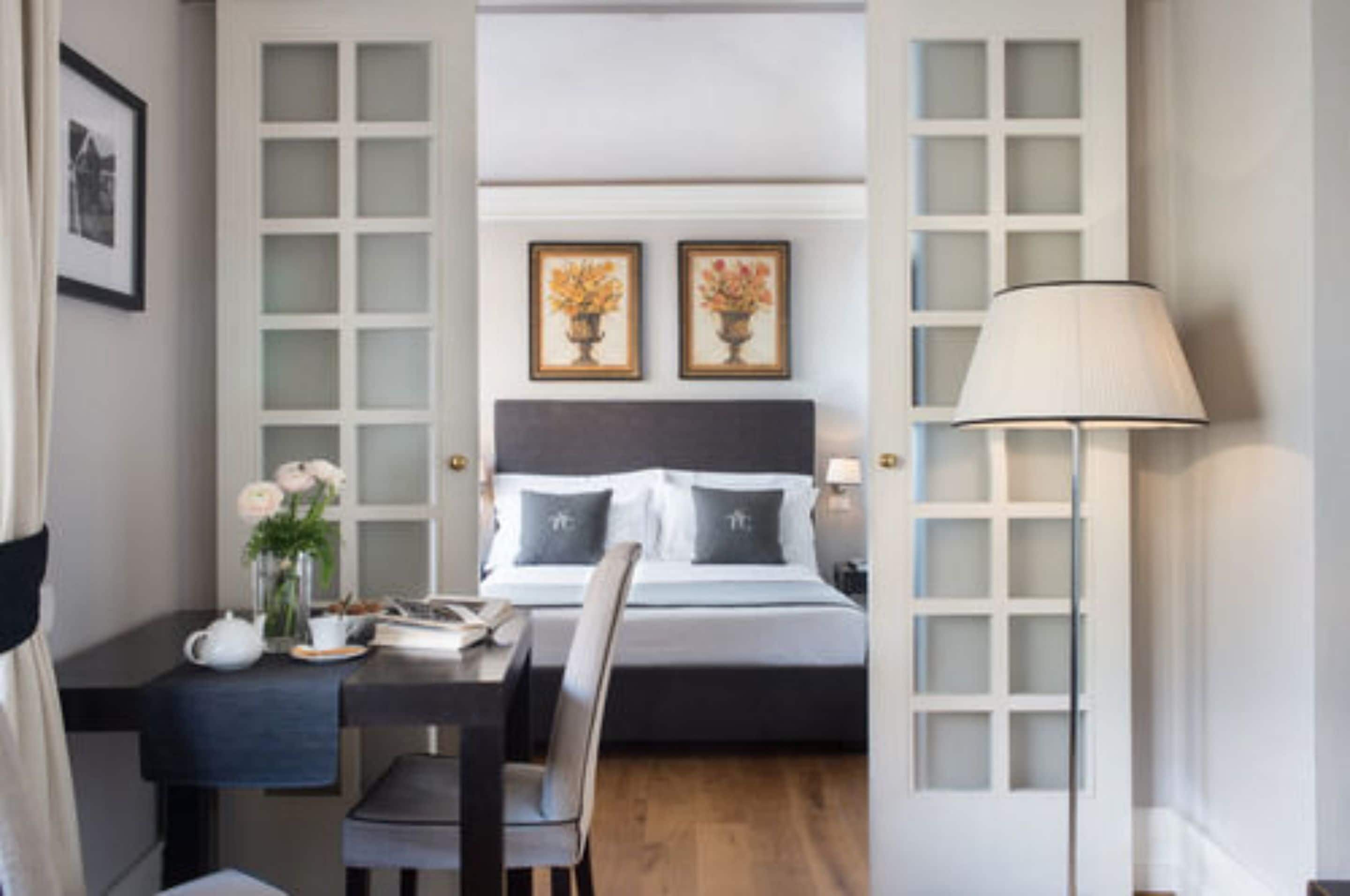 Une chambre d’hôtel comprenant un lit, des tables de chevet, un bureau avec une chaise, une lampe et des œuvres d’art encadrées accrochées au mur.