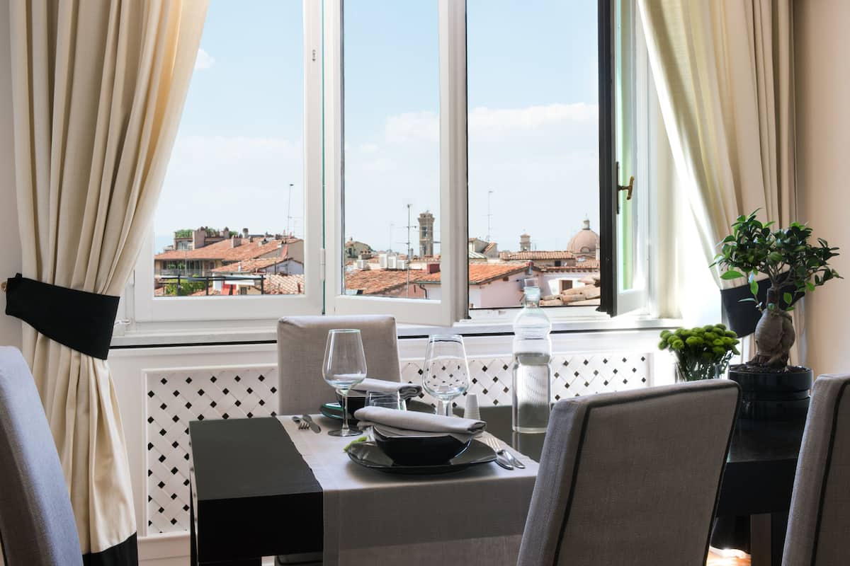 Mesa de jantar posta com garrafa, copos e tigela, com vista para edifícios e uma cúpula ao fundo.
