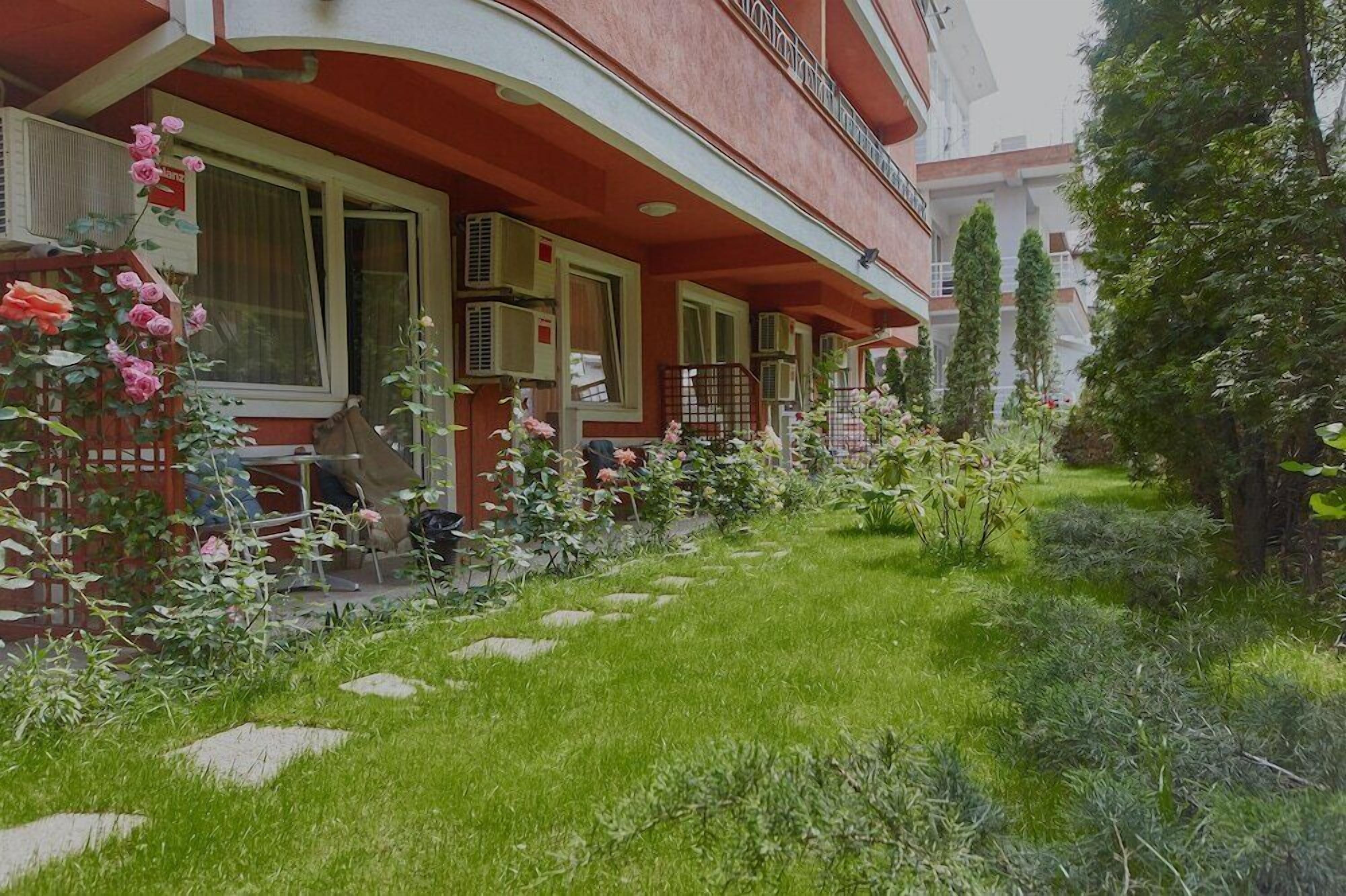 A building with a red facade, a covered outdoor seating area, and a garden with various plants and flowers.