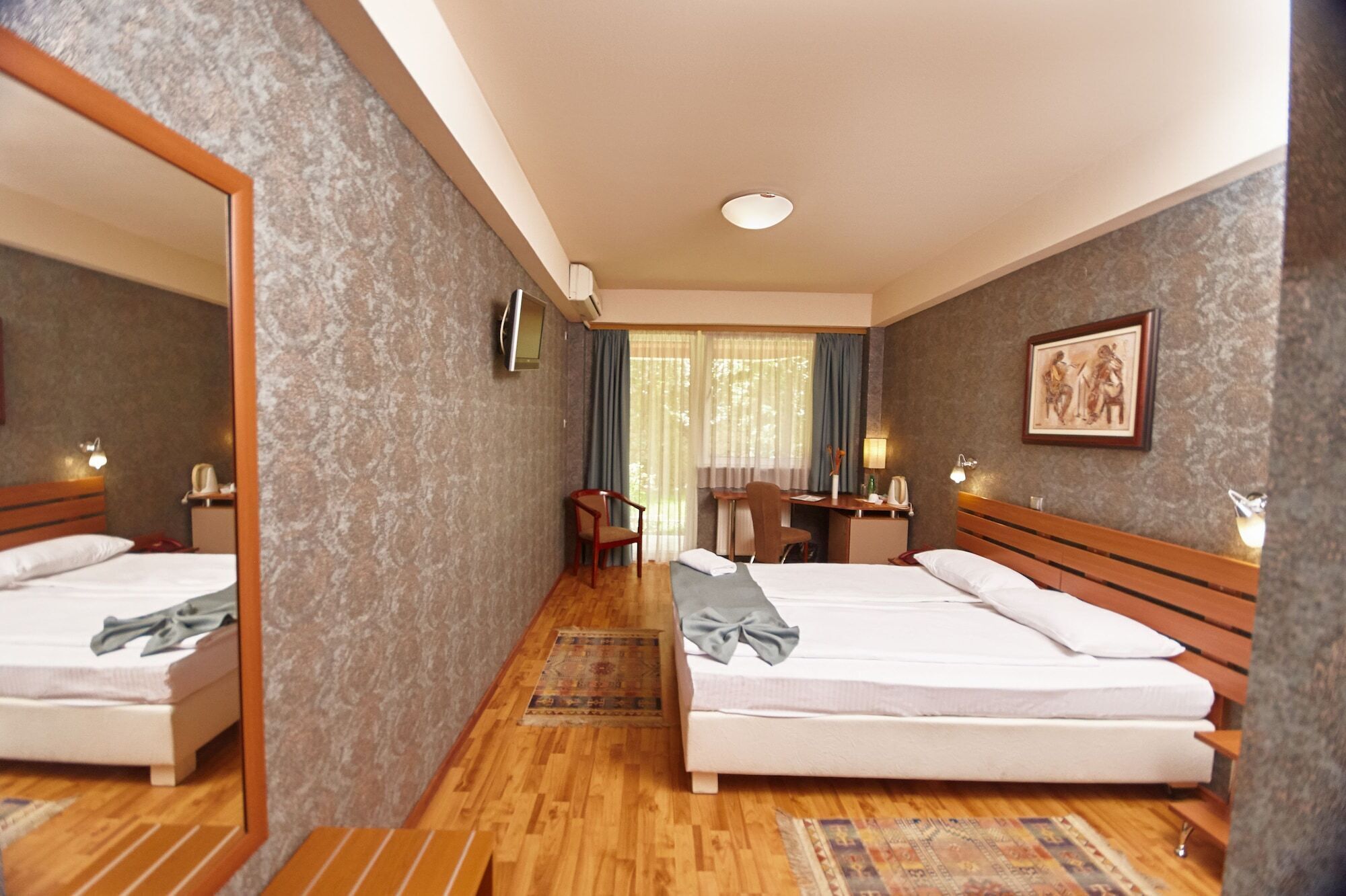 Une chambre d’hôtel avec deux lits, un bureau, une chaise, un miroir et un tableau au mur.