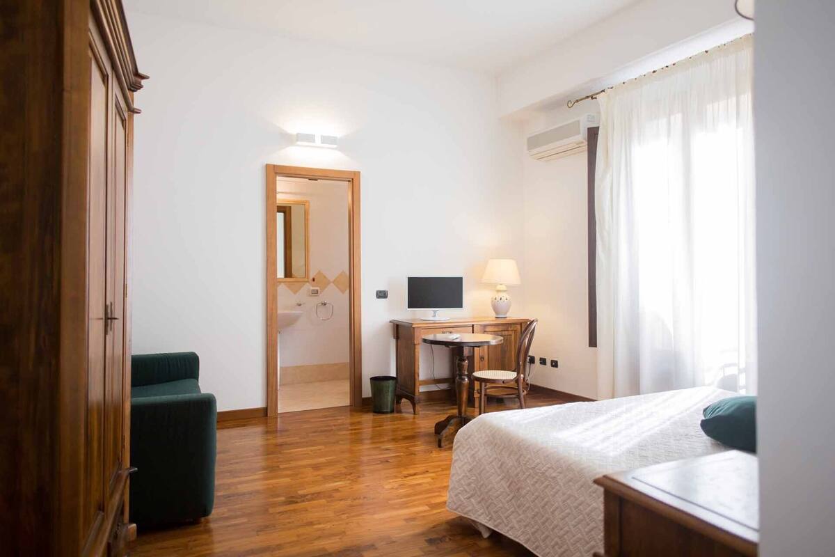 Ein Hotelzimmer mit einem Bett, einem Schreibtisch mit Lampe, einem Sessel und einem Kleiderschrank.
