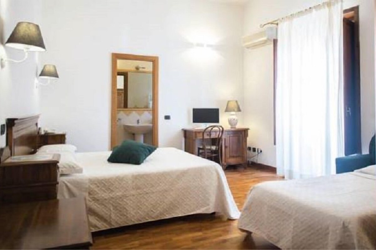 Een hotelkamer met twee bedden, een bureau met een computer, een spiegel en een raam met gordijnen.