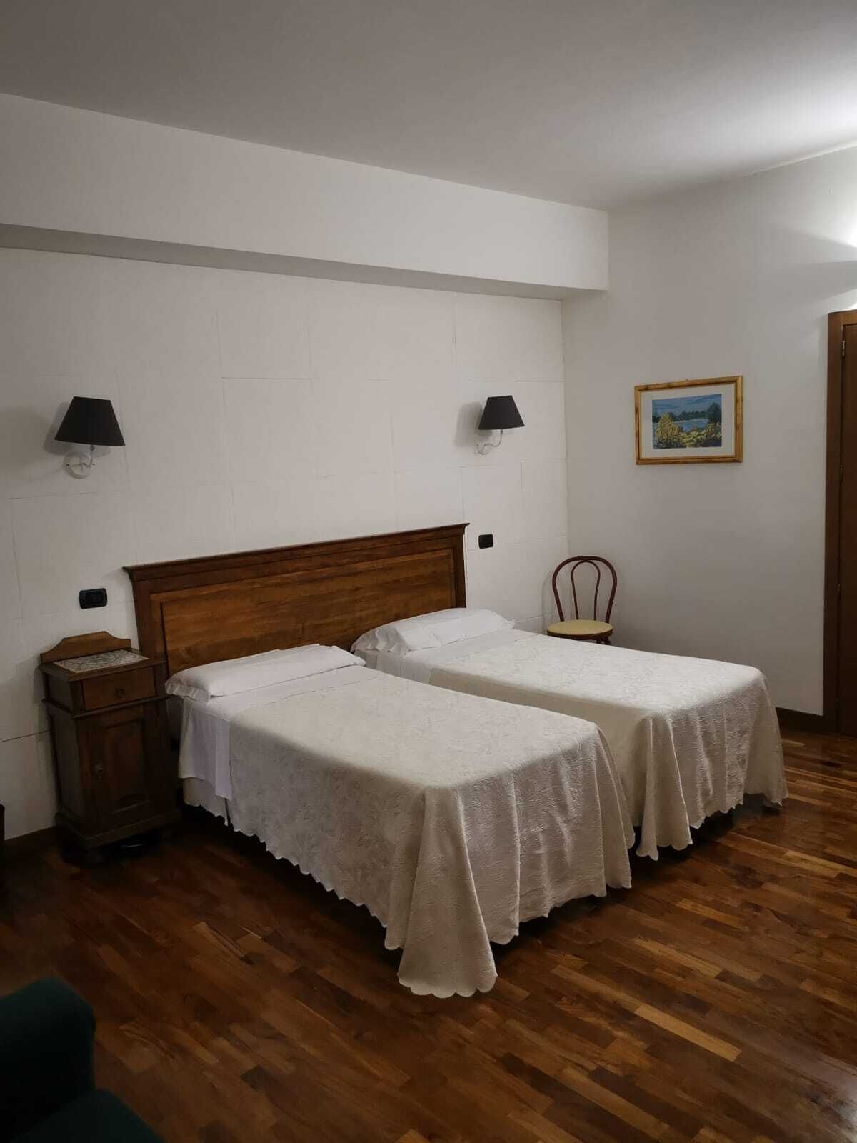 Una habitación con dos camas individuales, cabecera de madera, mesita de noche, una silla y un cuadro en la pared.