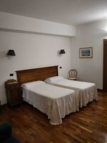 Una habitación con dos camas individuales, cabecera de madera, mesita de noche, una silla y un cuadro en la pared.